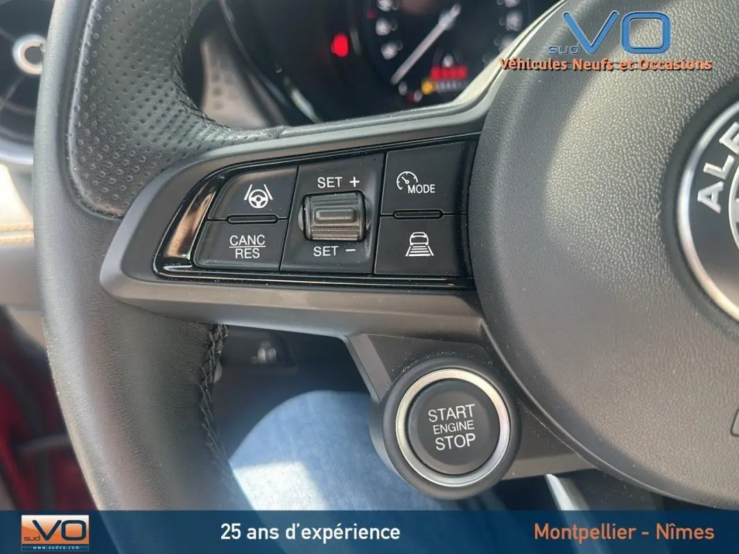 Gros plan sur le volant sport de l'Alfa Romeo Tonale rouge 2024, montrant les commandes du régulateur et le bouton start/stop.