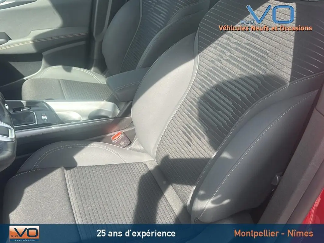 Vue rapprochée des sièges avant gris foncé de l'Alfa Romeo Tonale rouge, mettant en valeur l'accoudoir central et la console.