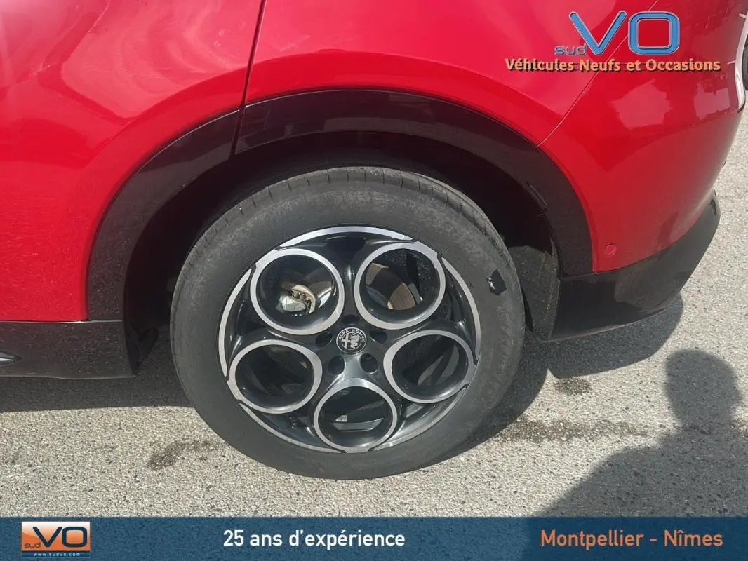 Gros plan sur la roue arrière droite rouge d'une Alfa Romeo Tonale 1.5 Hybrid Sprint avec jante noire à cercles argentés.