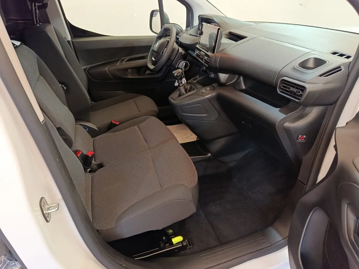 Vue intérieure côté conducteur du Peugeot Partner blanc 2026, montrant sièges tissu gris et tableau de bord moderne.