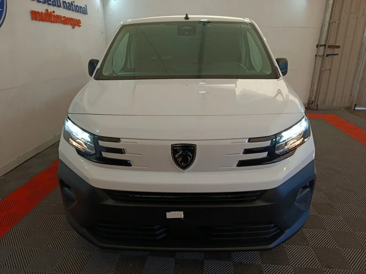 Vue avant d'un Peugeot Partner blanc 2026 avec phares allumés et calandre noire distinctive.