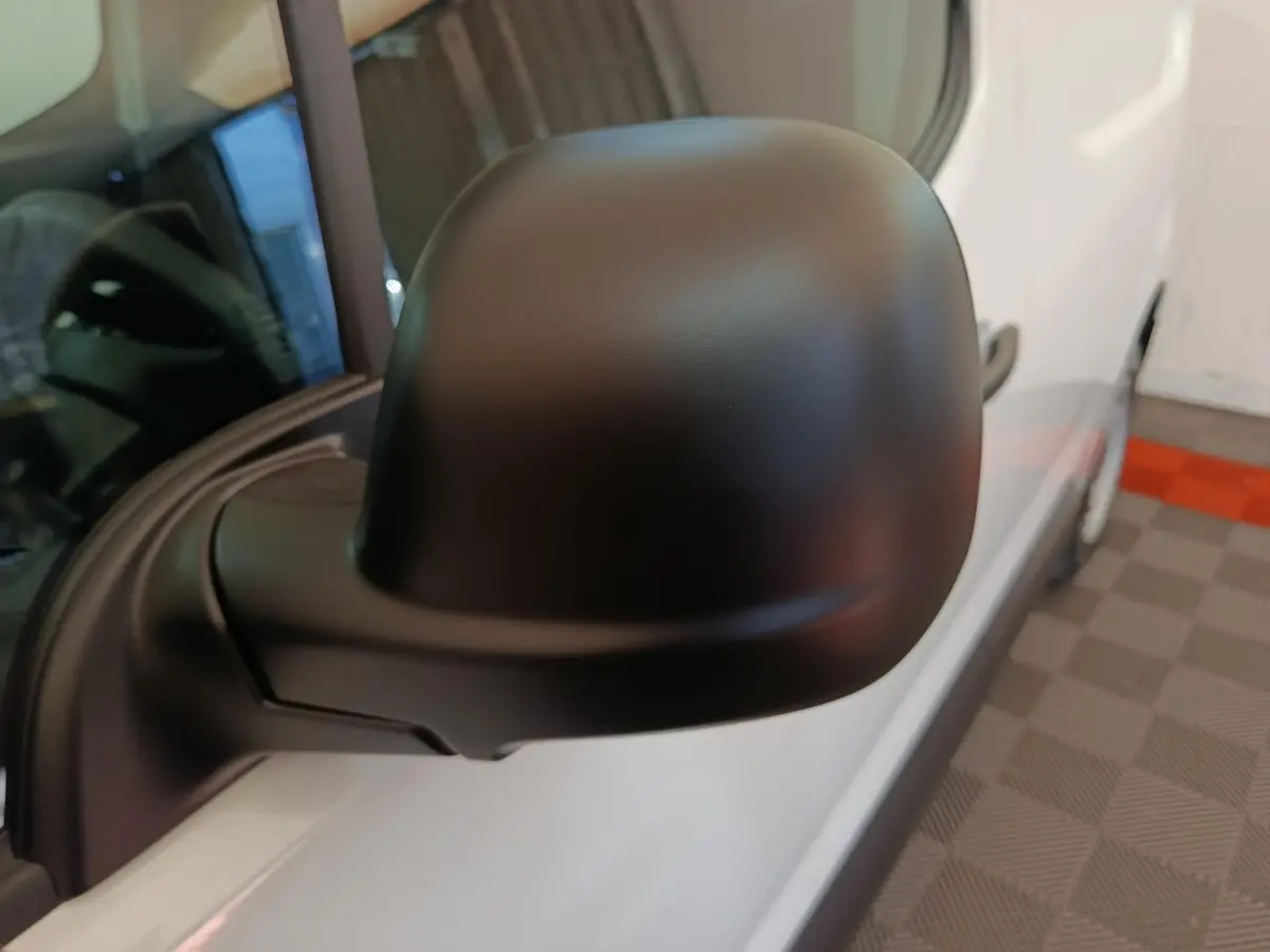 Gros plan sur le rétroviseur noir côté conducteur d’un Peugeot Partner blanc, vue avant droite partielle.