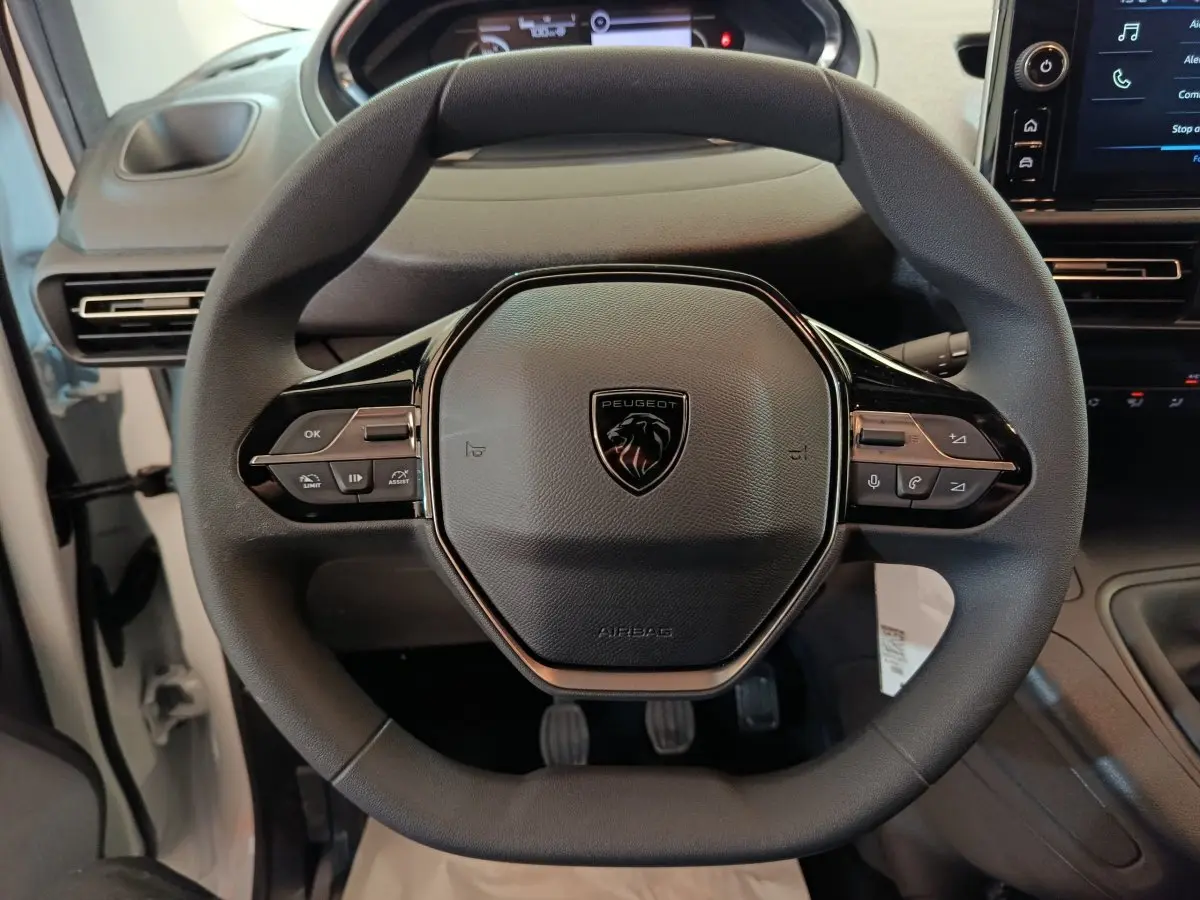 Vue rapprochée du volant noir du Peugeot Partner 2026 avec commandes intégrées et tableau de bord partiellement visible.