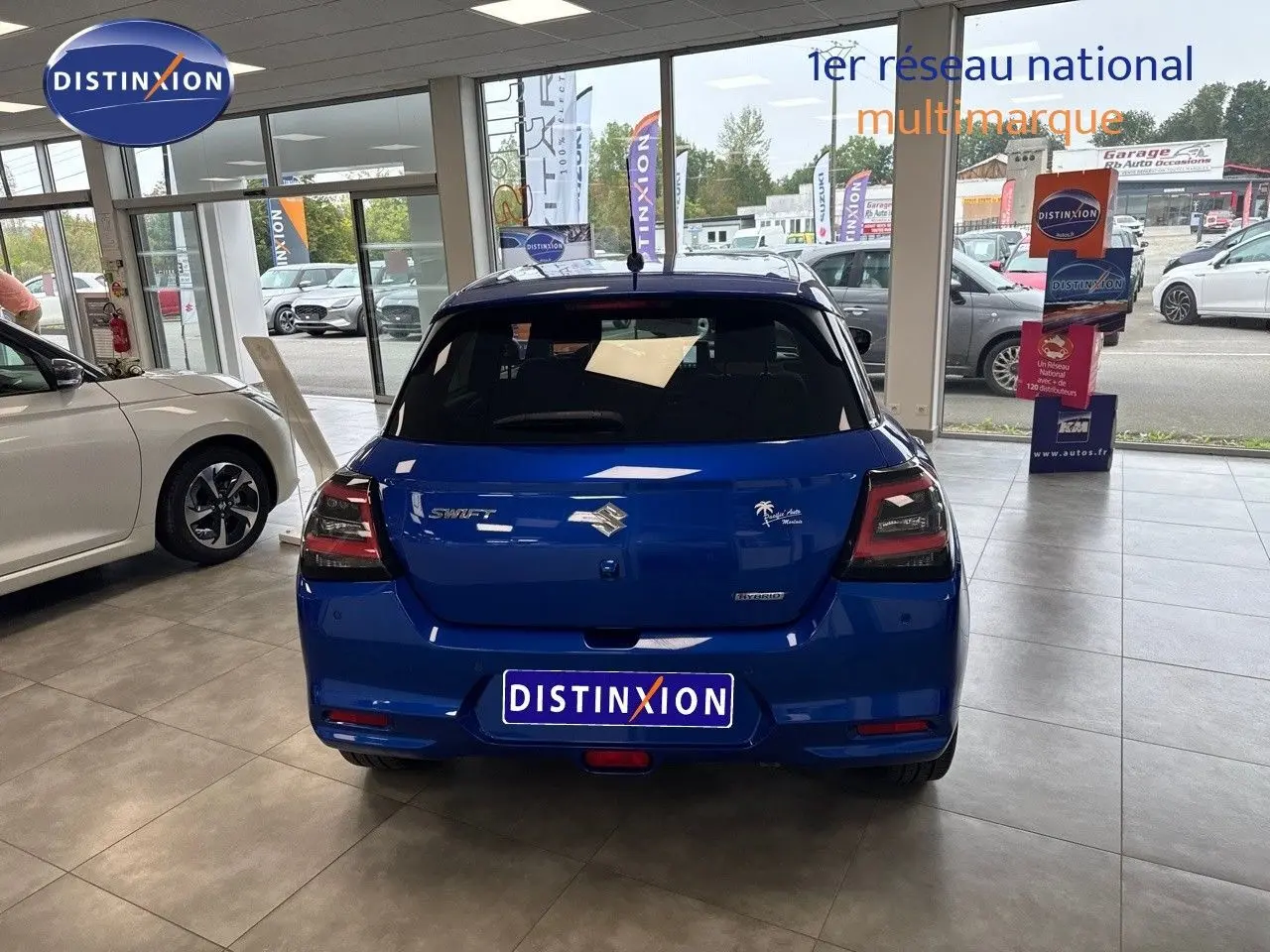 Vue arrière d'une Suzuki Swift 1.2 Pack Hybrid bleu exposée en showroom avec feux arrière fumés et logo distinctif.