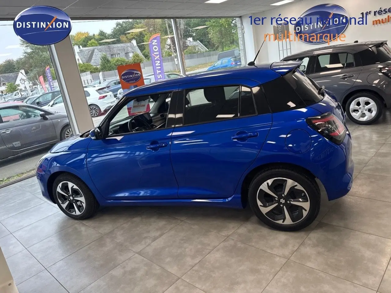 Vue de profil côté gauche d'une Suzuki Swift 1.2 Pack Hybrid bleu, en showroom avec jantes distinctives noires et argent.