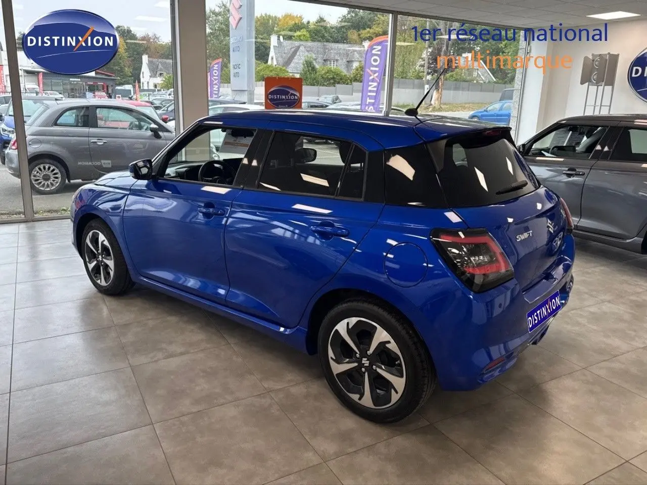 Suzuki Swift 1.2 Pack Hybrid bleu vue 3/4 arrière droit en intérieur, avec jantes alliage et vitres teintées.
