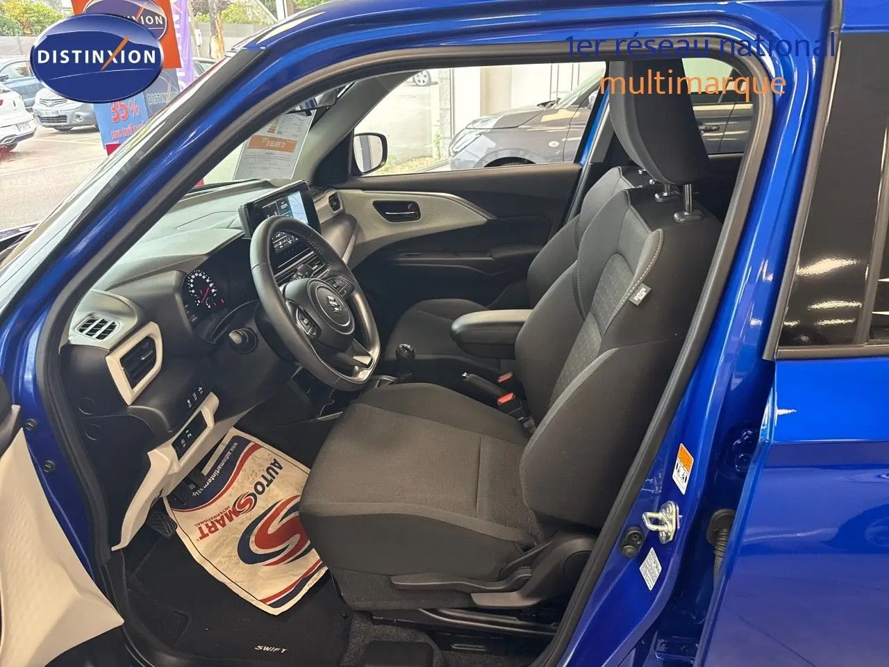 Intérieur de la Suzuki Swift 1.2 Pack Hybrid 2024 en bleu, vue côté conducteur avec tableau de bord et sièges noirs.