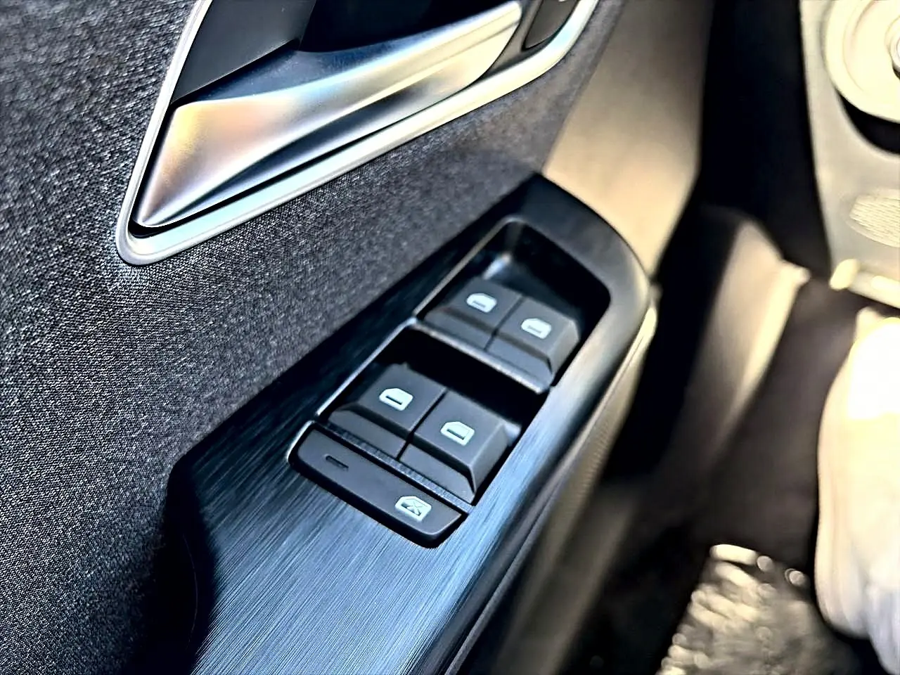 Gros plan sur les commandes des vitres électriques côté gauche d’une MG ZS noire, avec poignée de porte argentée.