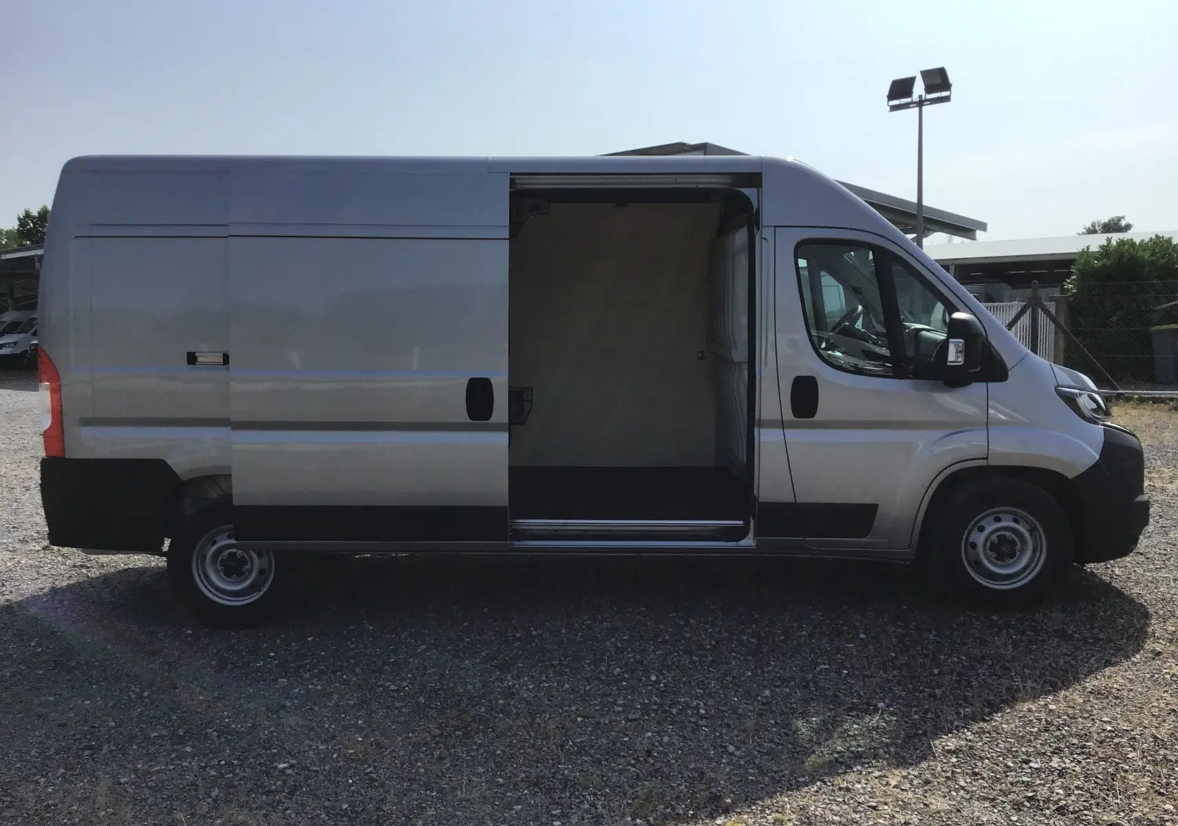 Profil droit du Peugeot Boxer Fourgon gris Artense 2025 avec porte latérale coulissante ouverte sur zone de chargement.