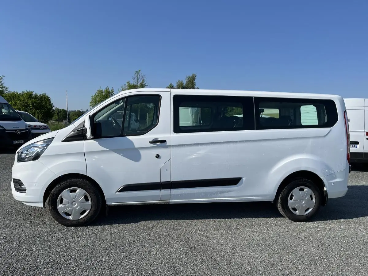 Profil côté gauche d'un Ford Transit Custom Kombi blanc, avec fenêtres latérales et jantes acier.