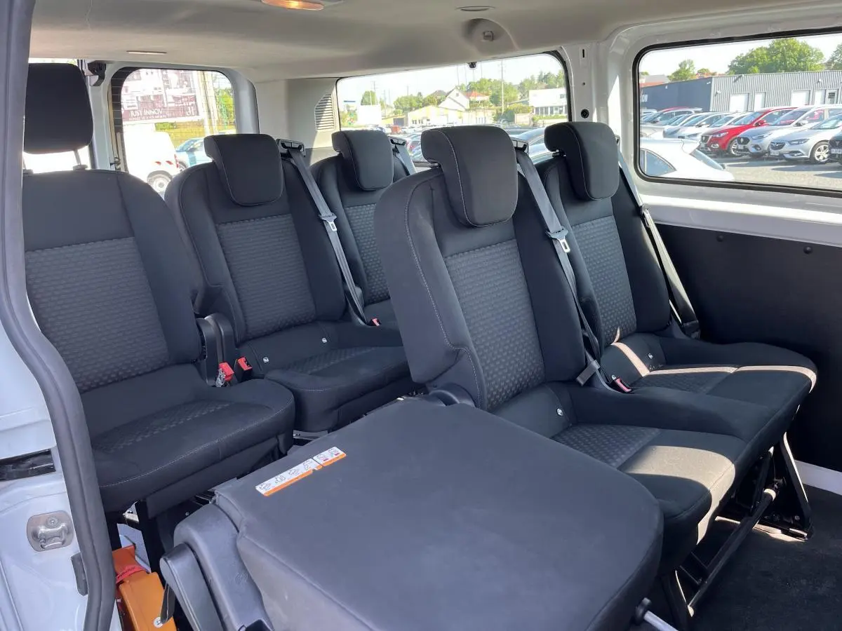 Vue intérieure côté droit du Ford Transit Custom Kombi blanc, montrant les banquettes arrière noires et les ceintures de sécurité.