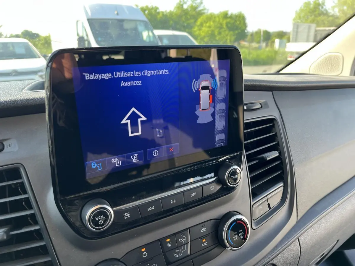 Vue rapprochée de l'écran tactile central du Ford Transit Custom blanc, affichant l'assistance au stationnement active.