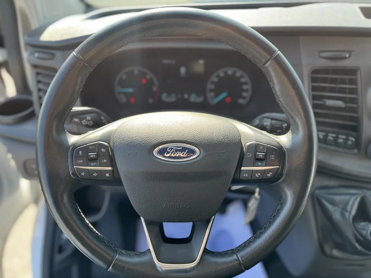 Volant en cuir noir de Ford Transit Custom 2021 avec commandes intégrées et tableau de bord en arrière-plan flou.