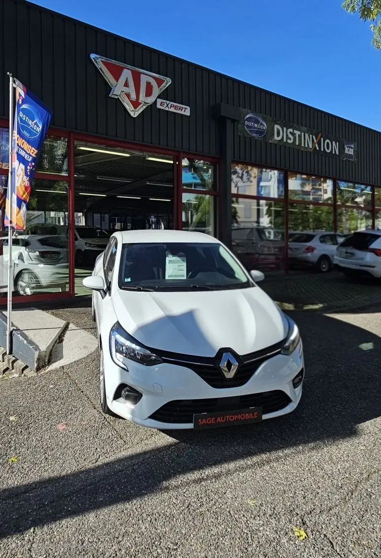 Renault Clio blanc glacier vue de face, stationnée devant un garage avec enseigne AD Expert.