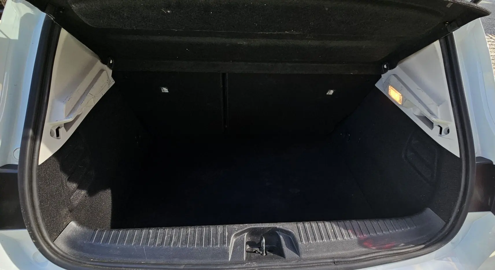 Coffre ouvert vu de l'arrière d'une Renault Clio blanche Glacier hybride, montrant l'espace de chargement vide et l'éclairage intérieur.