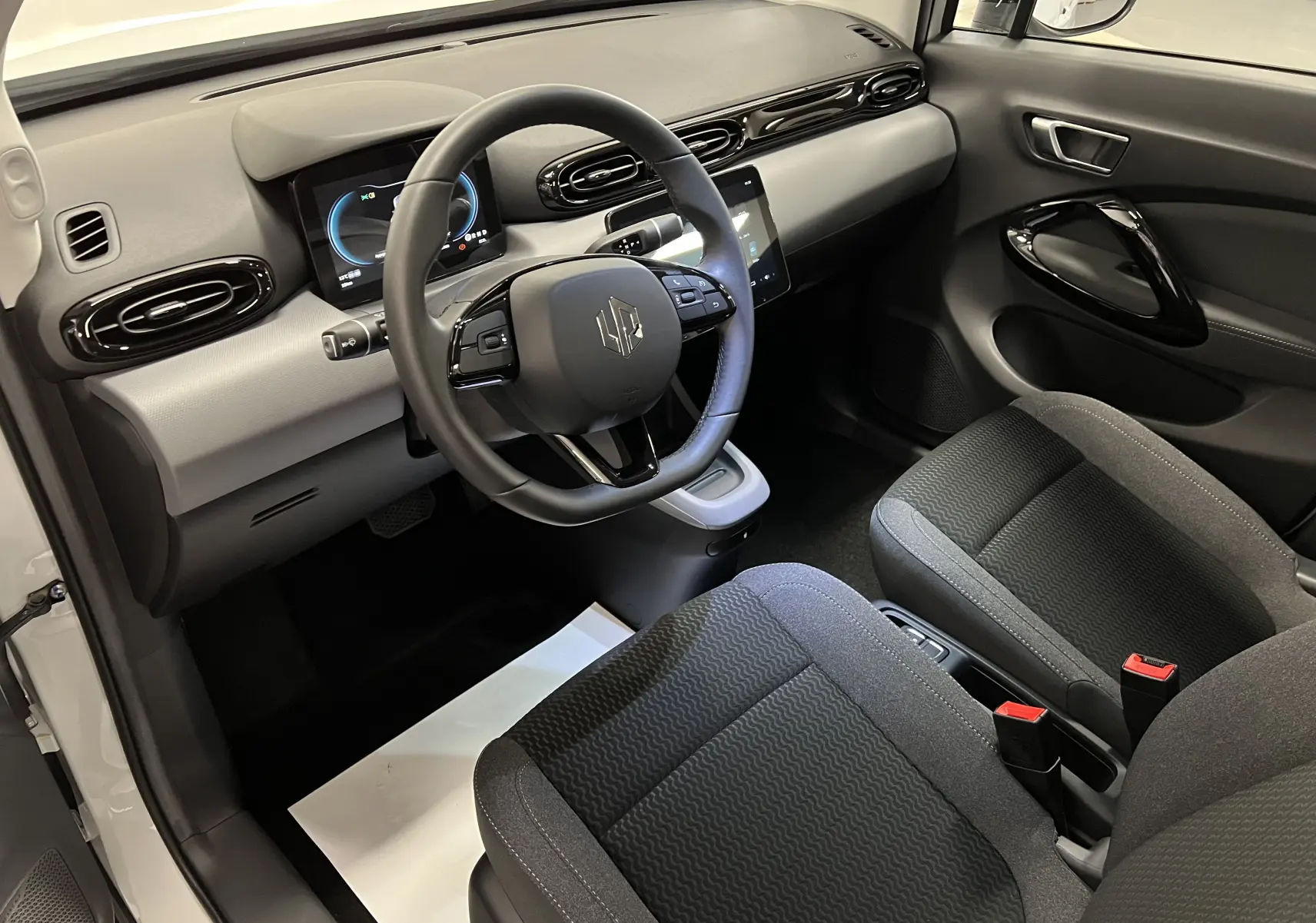 Intérieur de la Renault ZOE blanc 2024, vue côté conducteur, tableau de bord moderne avec écran digital et sièges tissu noirs.