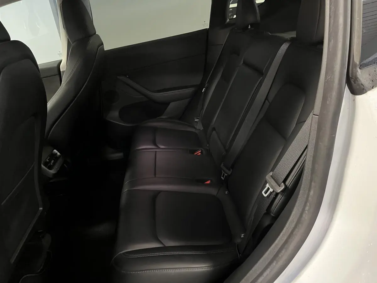 Vue côté droit des sièges arrière noirs en cuir du Tesla Model Y blanc 2022, avec ceintures de sécurité visibles.