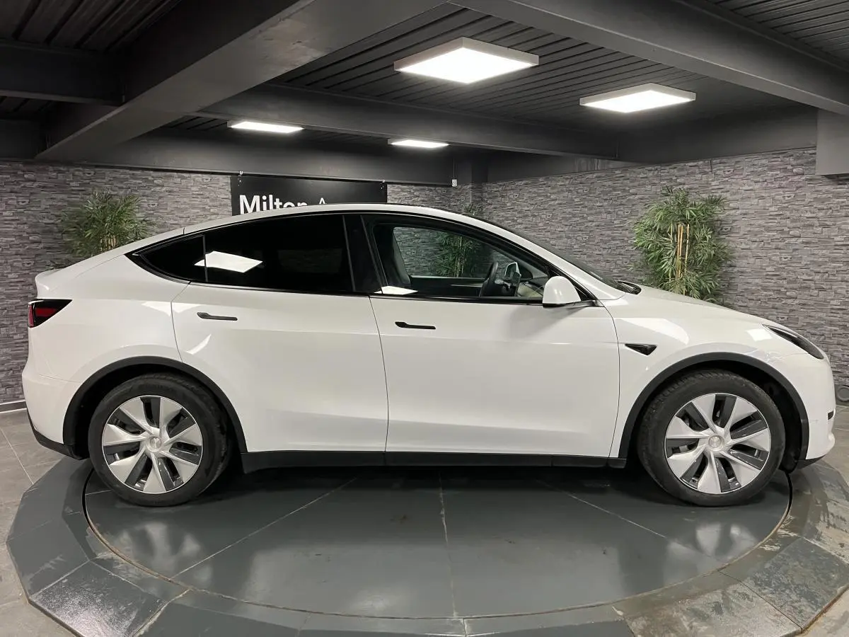 Profil côté gauche d'une Tesla Model Y blanche 2022 RWD Autonomie Standard en intérieur avec jantes alu.