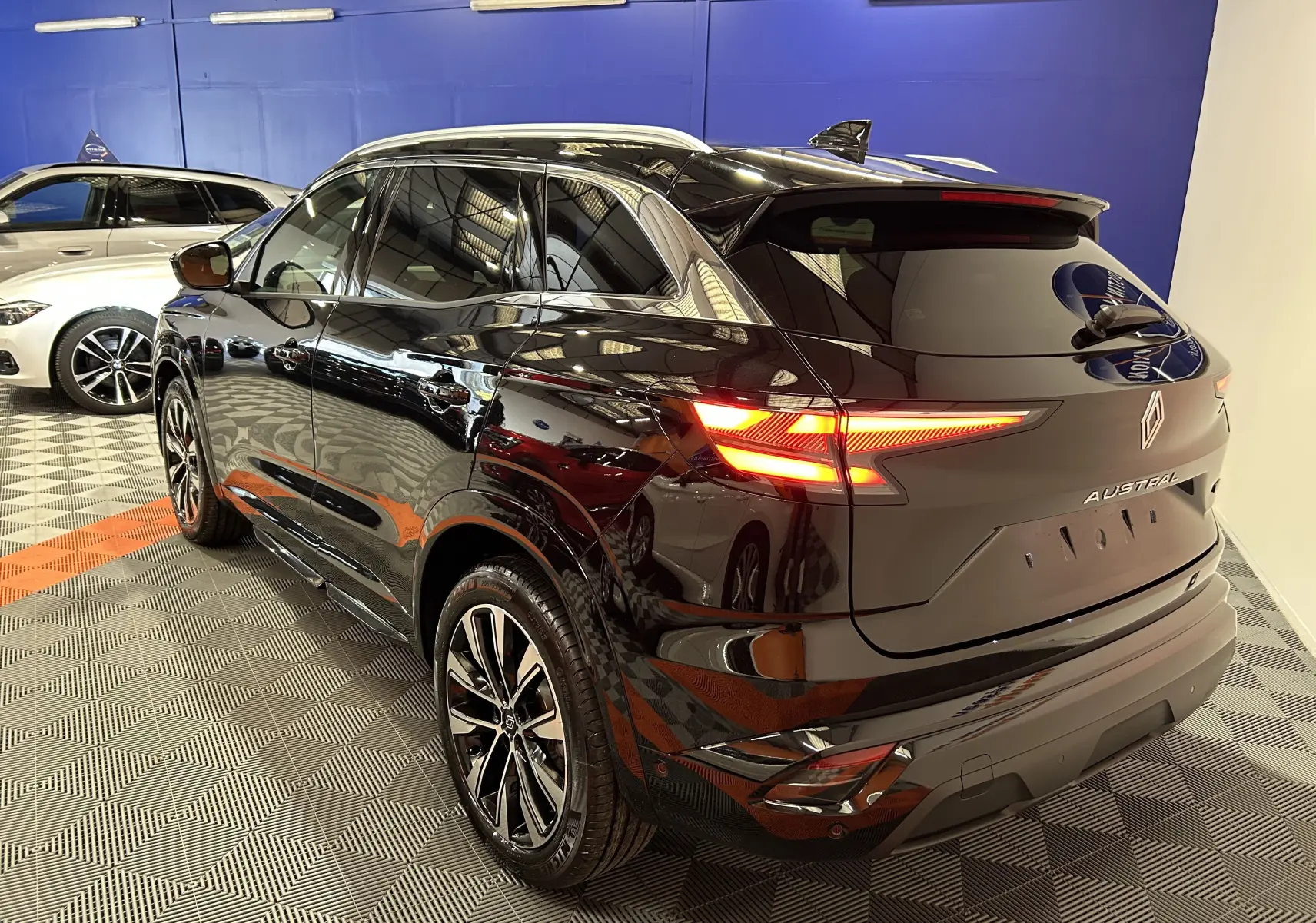 Vue 3/4 arrière droite d'un Renault Austral noir étoilé avec feux arrière allumés et hayon électrique visible.