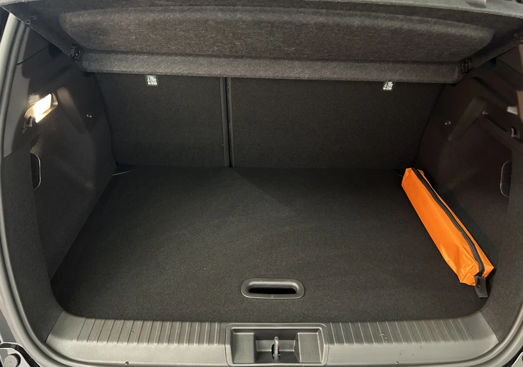 Coffre ouvert du Renault Captur II Ph.2 TECHNO noir étoilé, montrant un espace de rangement propre avec une trousse orange sur la droite.