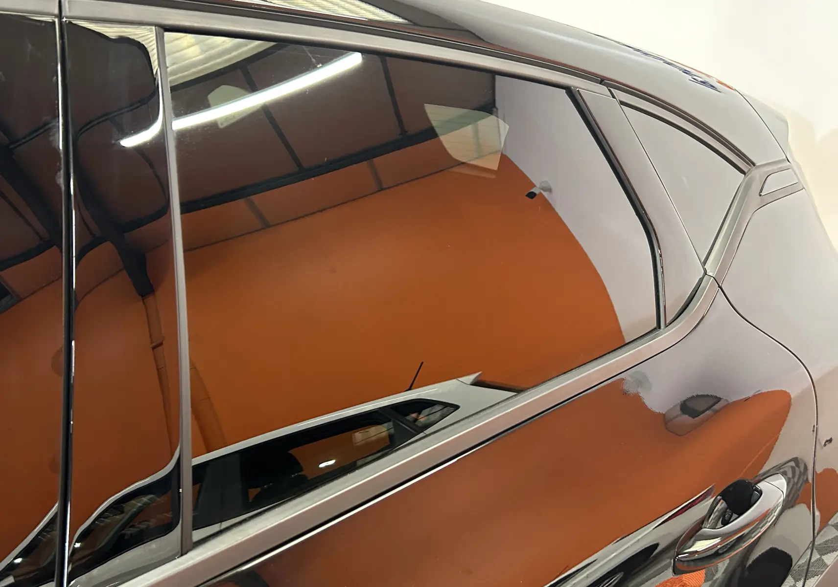 Détail sur la porte arrière côté gauche d'un Renault Captur II Ph.2 noir étoilé avec reflet intérieur orange.