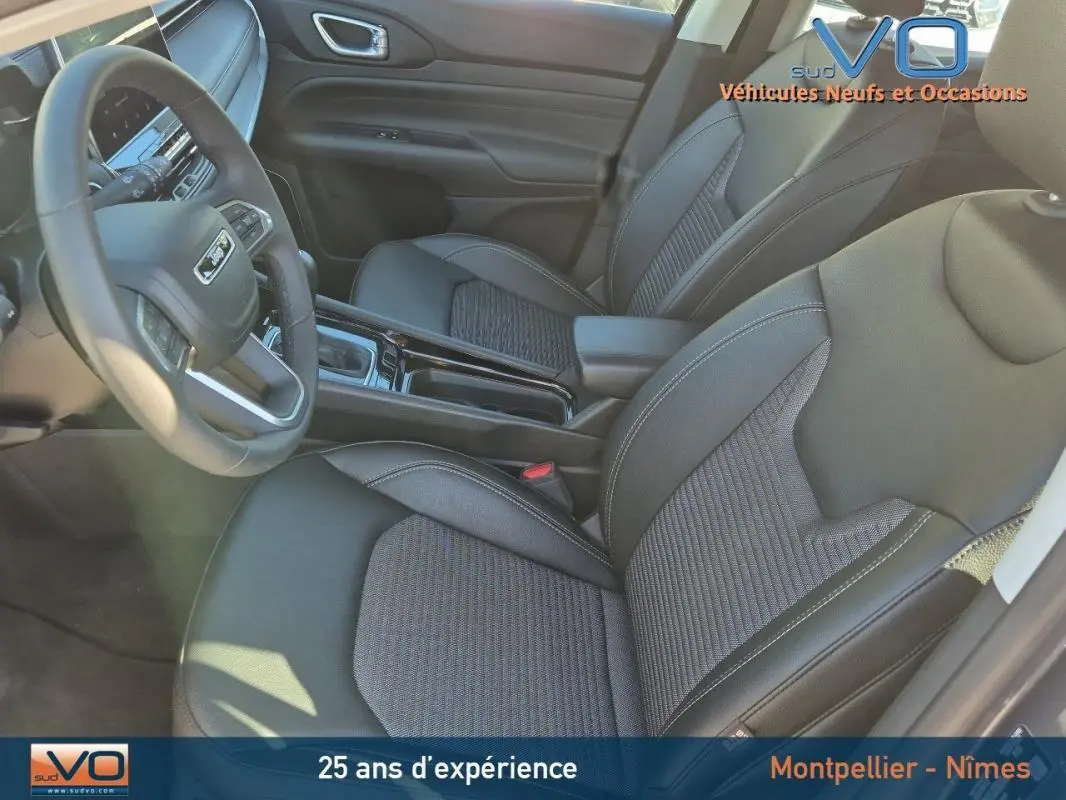 Vue intérieure côté conducteur du Jeep Compass 2024 gris, montrant sièges en tissu et cuir avec accoudoir central.