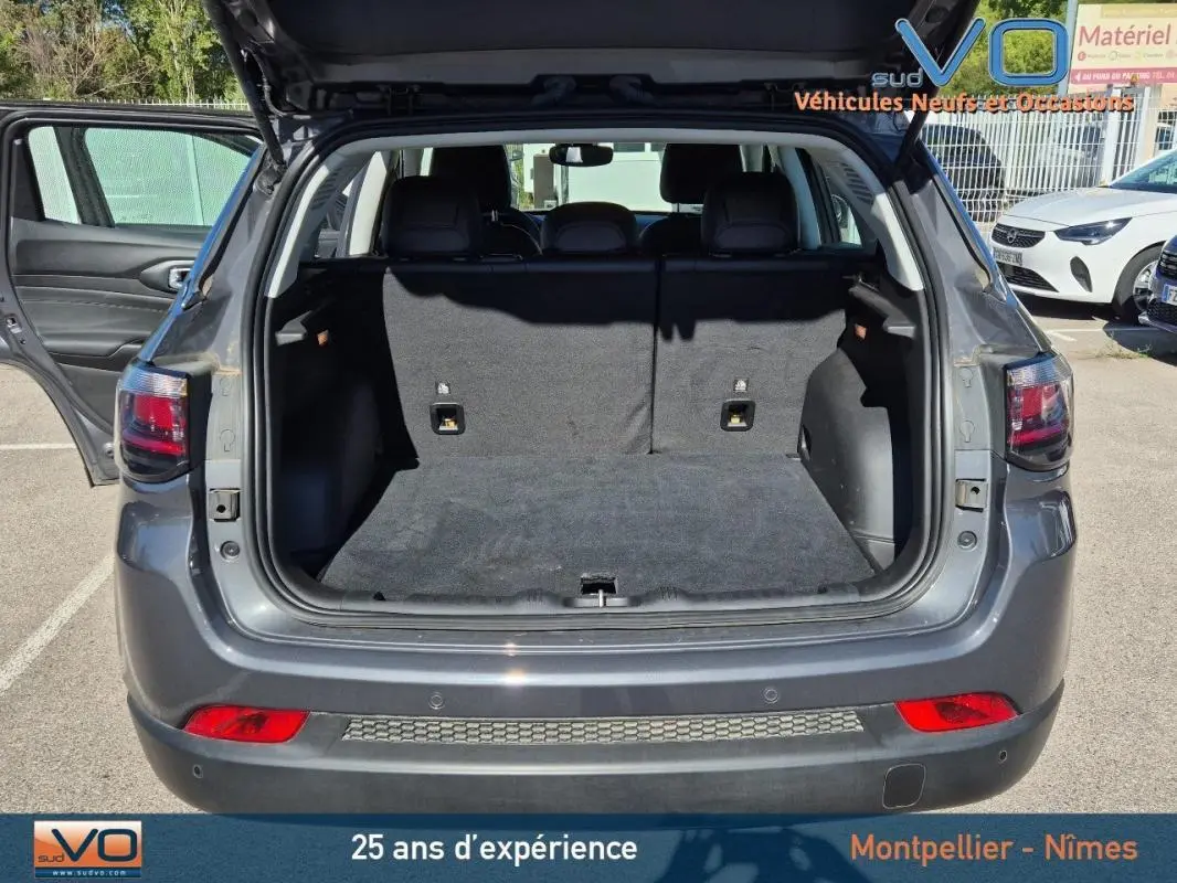 Coffre ouvert d'un Jeep Compass gris 3/4 arrière, montrant l'espace de chargement et la porte arrière relevée.