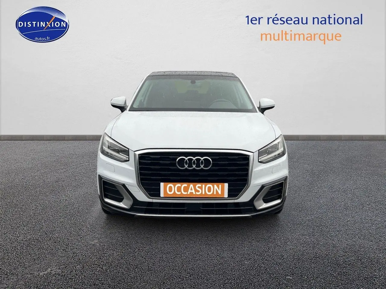 Vue avant d'un Audi Q2 blanc Ibis avec calandre noire et plaque orange "OCCASION" sur un sol gris.