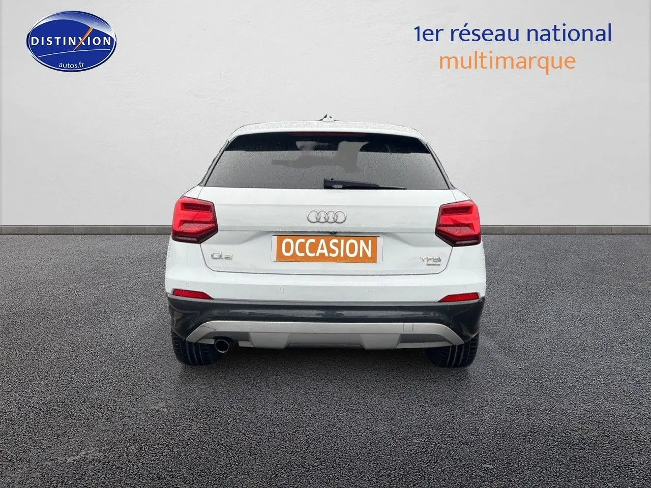 Vue arrière d'un Audi Q2 blanc Ibis avec feux rouges et pare-chocs noir, sur fond gris neutre.