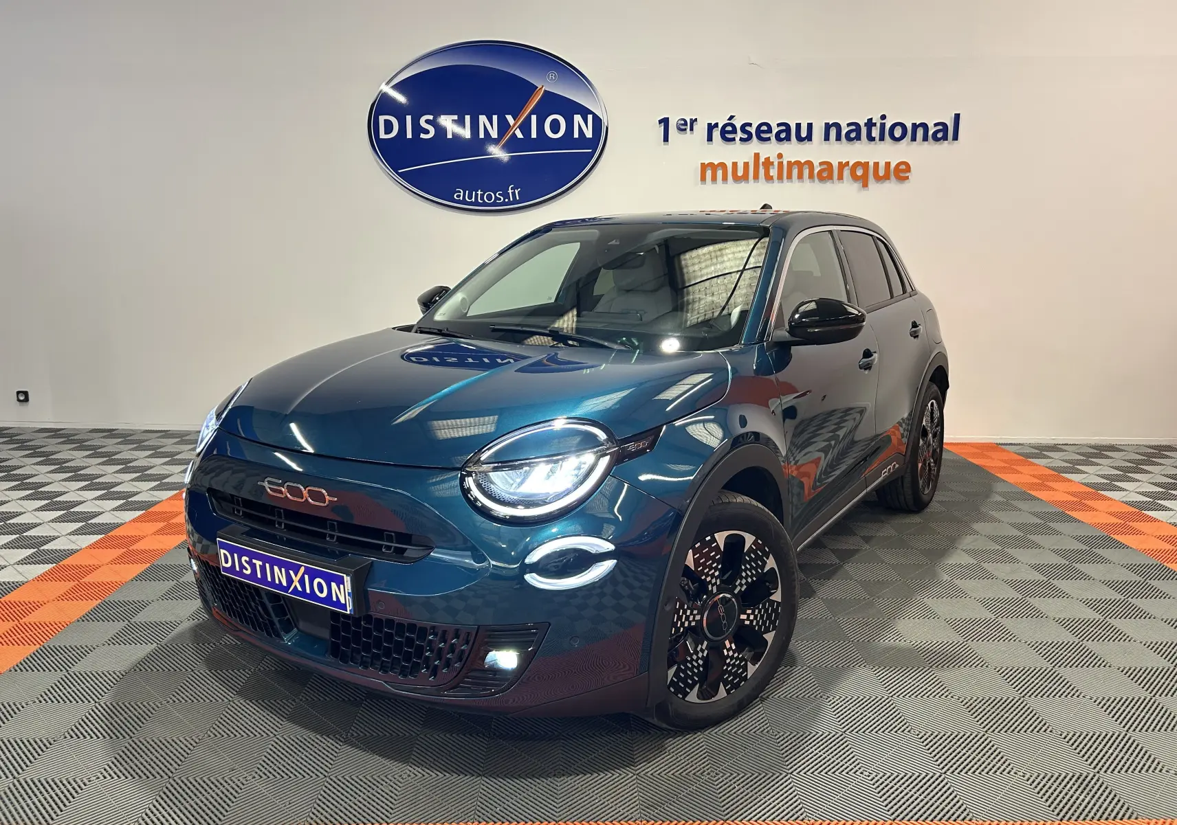 Vue 3/4 avant droite d'une FIAT 600 Hybrid 100 La Prima bleu métallisé avec phares LED allumés en showroom