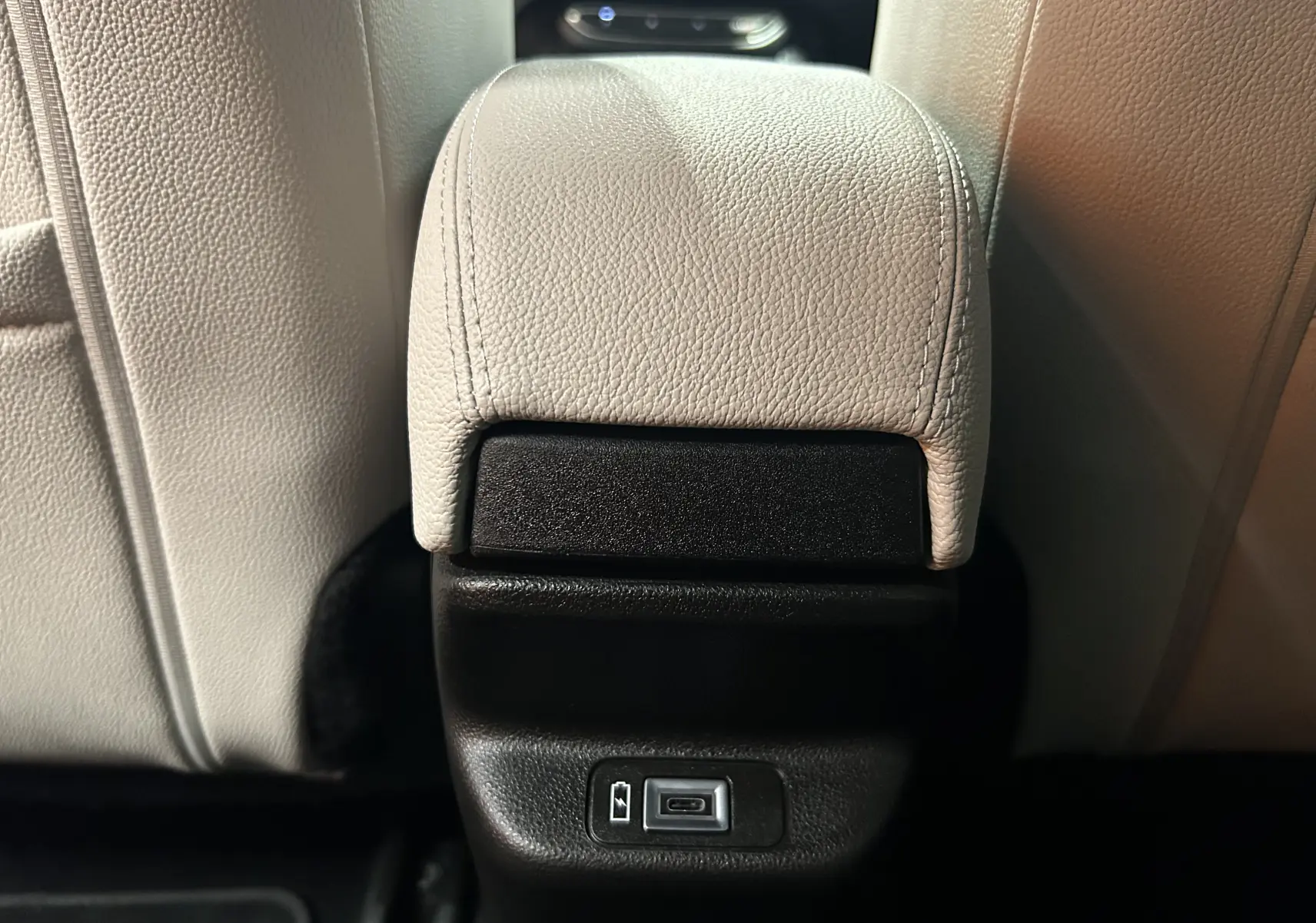 Prise USB en gros plan sur la console arrière entre les sièges en cuir beige d'une Fiat 600 Hybrid 2024.