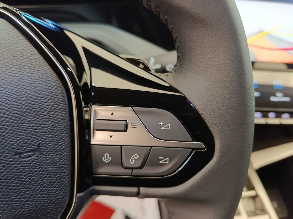 Gros plan sur les commandes du volant cuir gris de la Peugeot 308 BlueHDi 130, avec écran tactile en arrière-plan.