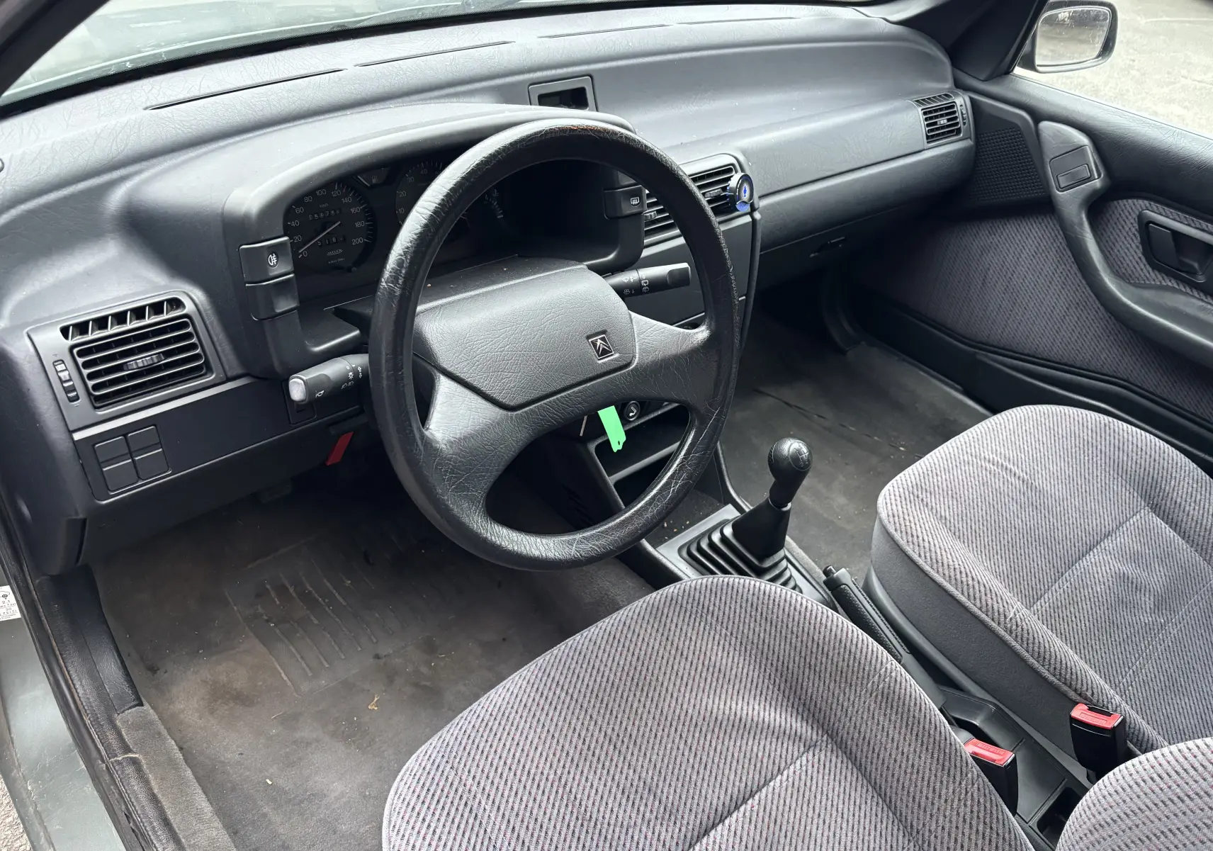 Intérieur côté conducteur de Citroën ZX 1.6i gris 1992, volant cuir, tableau de bord simple et sièges tissu rayé.