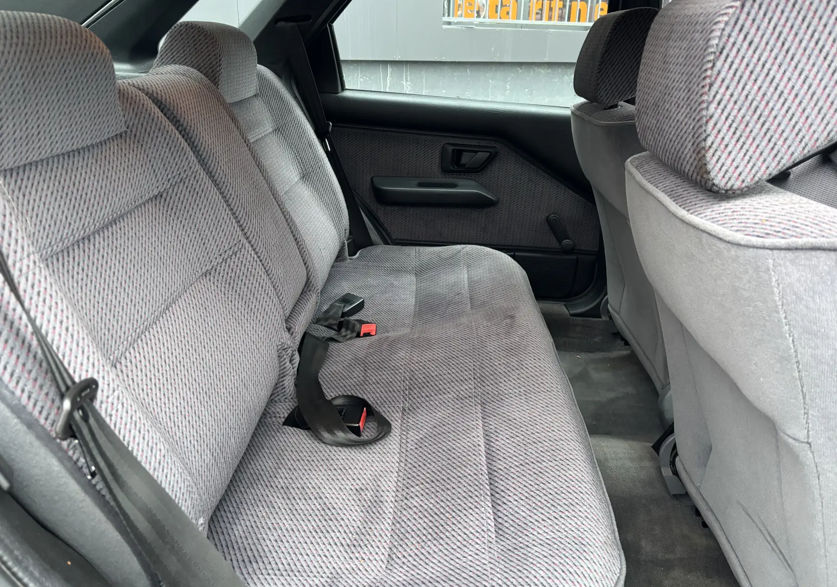 Vue intérieure arrière montrant la banquette en tissu gris à motifs de la Citroën ZX 1.6i de 1992.