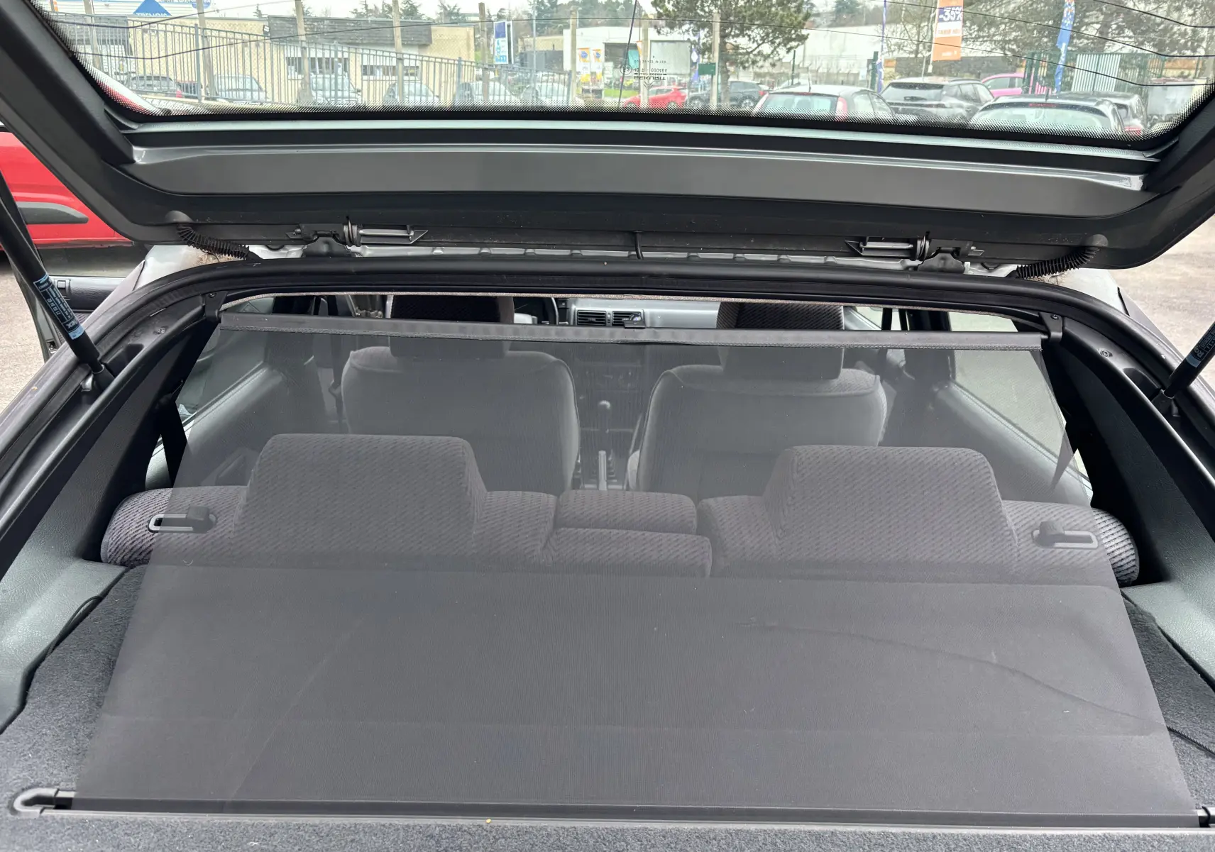 Vue arrière ouverte sur l'intérieur gris en tissu d'une Citroën ZX 1.6i 89CV de 1992 avec cache-bagages déployé.