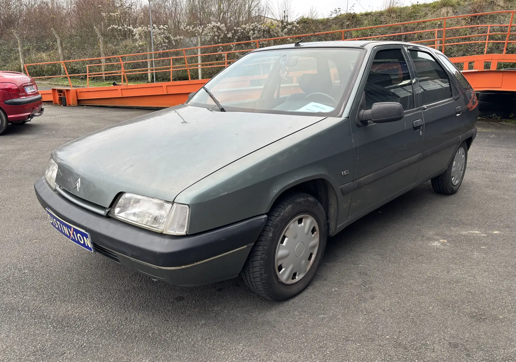 Citroën ZX 1.6i gris vue 3/4 avant droit, avec jantes pleines et rétroviseurs noirs sur parking extérieur.