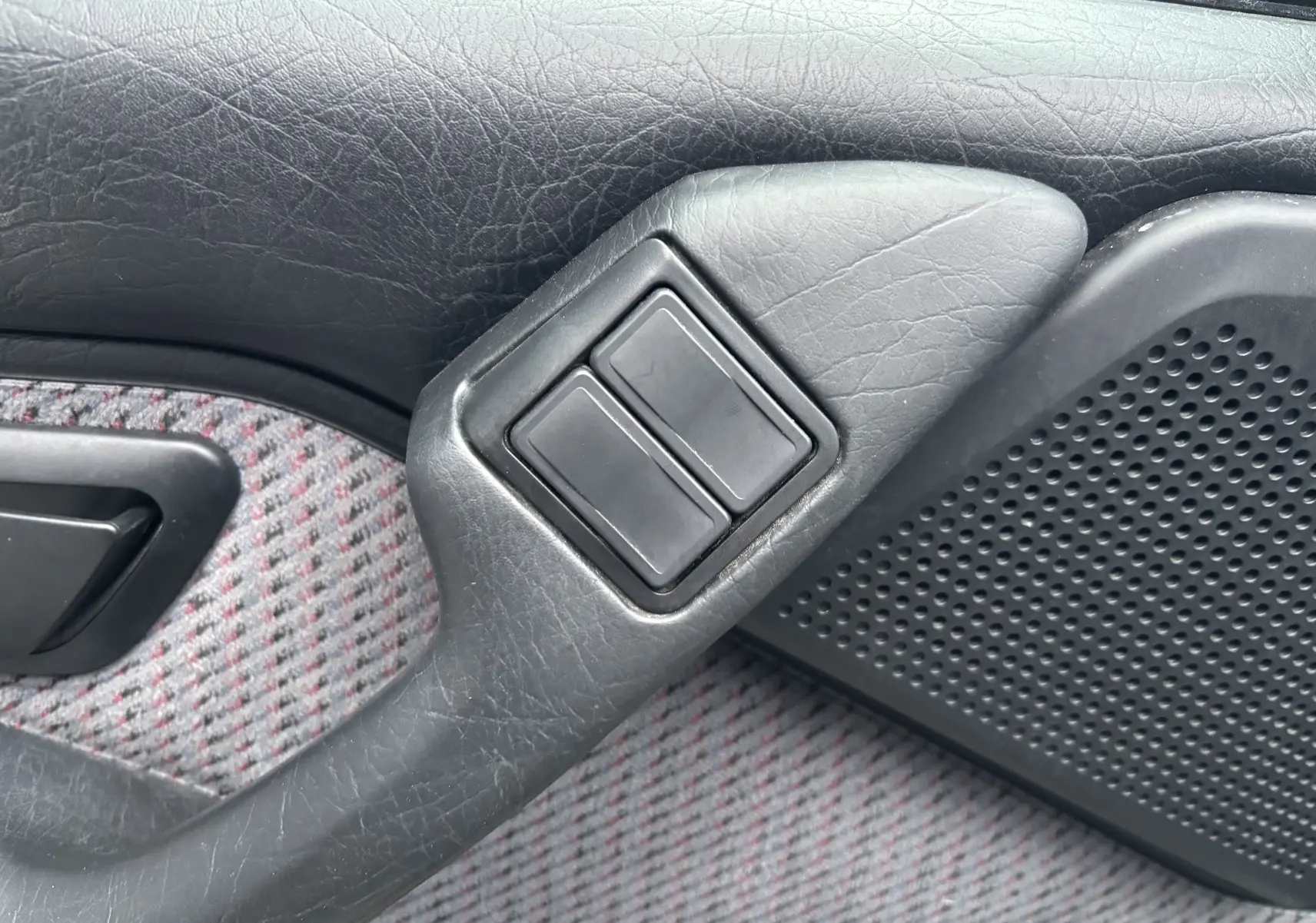 Détail des commandes électriques sur la porte côté gauche d'une Citroën ZX gris 1.6i de 1992 avec tissu à motifs.