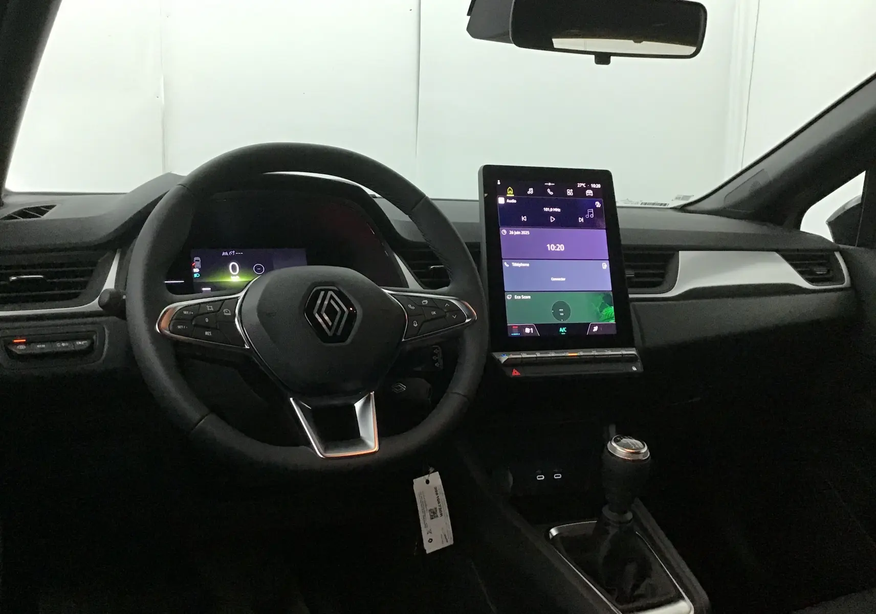 Intérieur du Renault Captur 2025 essence, vue centrée sur le volant multifonction et l'écran tactile vertical du tableau de bord.