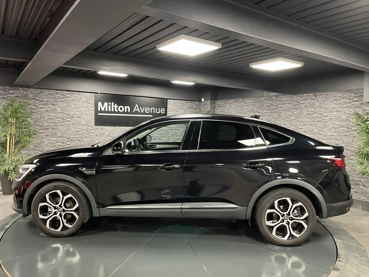 Profil côté gauche du Renault Arkana noir métal 2021 avec jantes alliage 18 pouces dans un showroom intérieur.