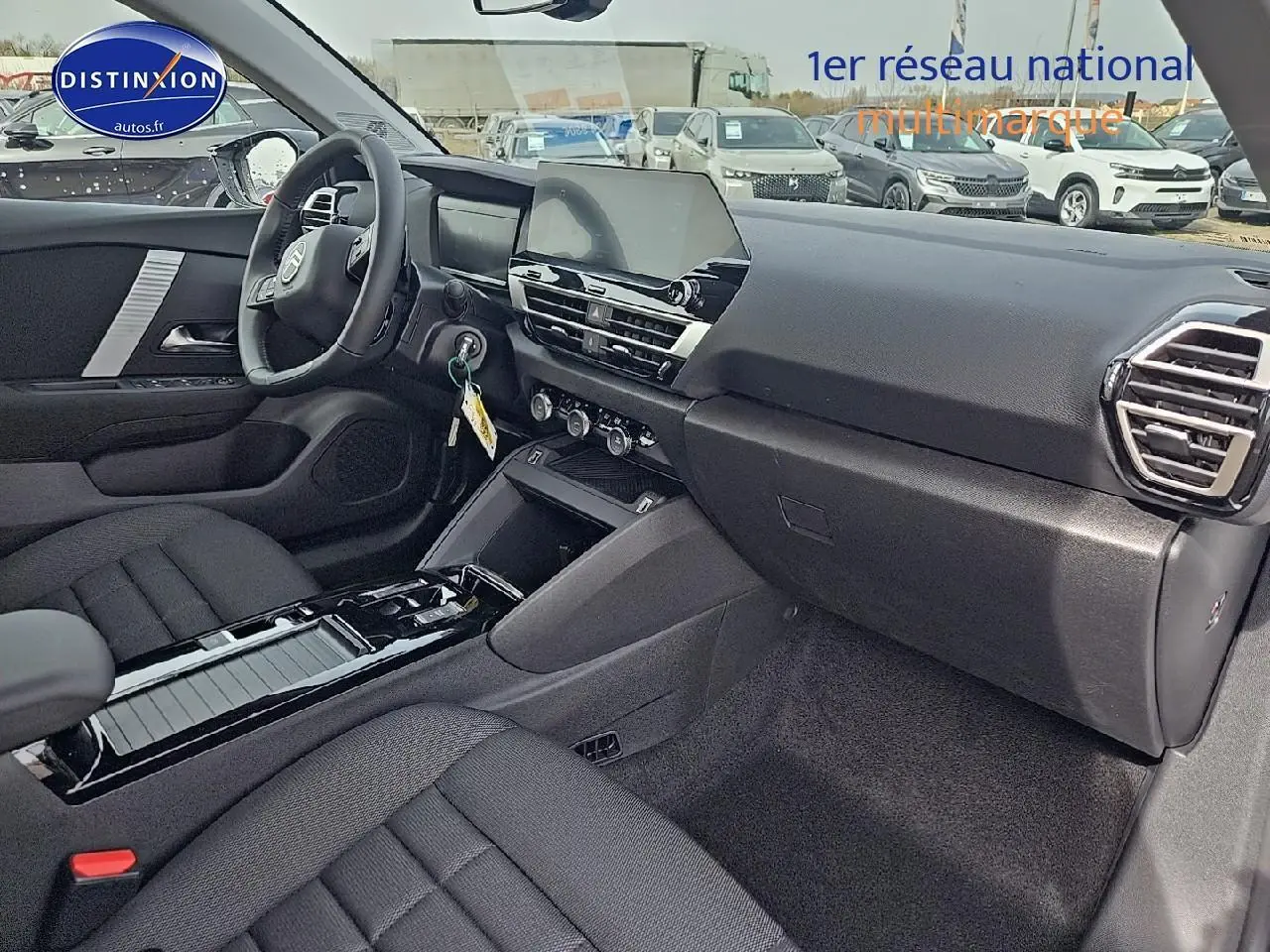 Vue intérieure côté passager de la Citroën C4 blanche, montrant tableau de bord noir et sièges tissu noir.