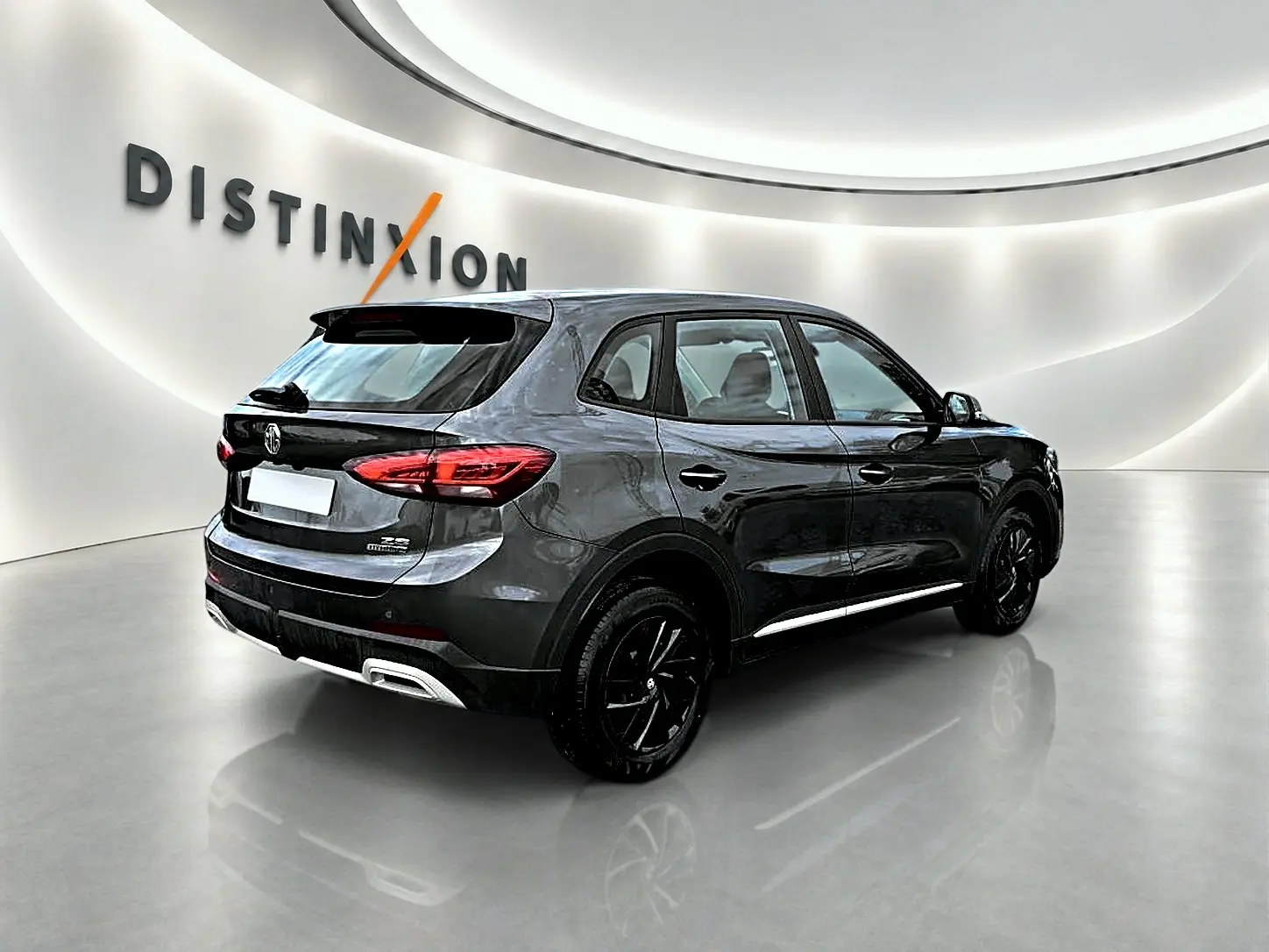 Vue 3/4 arrière droite du MG ZS Camden grey 2026 avec jantes noires et becquet arrière en showroom lumineux.