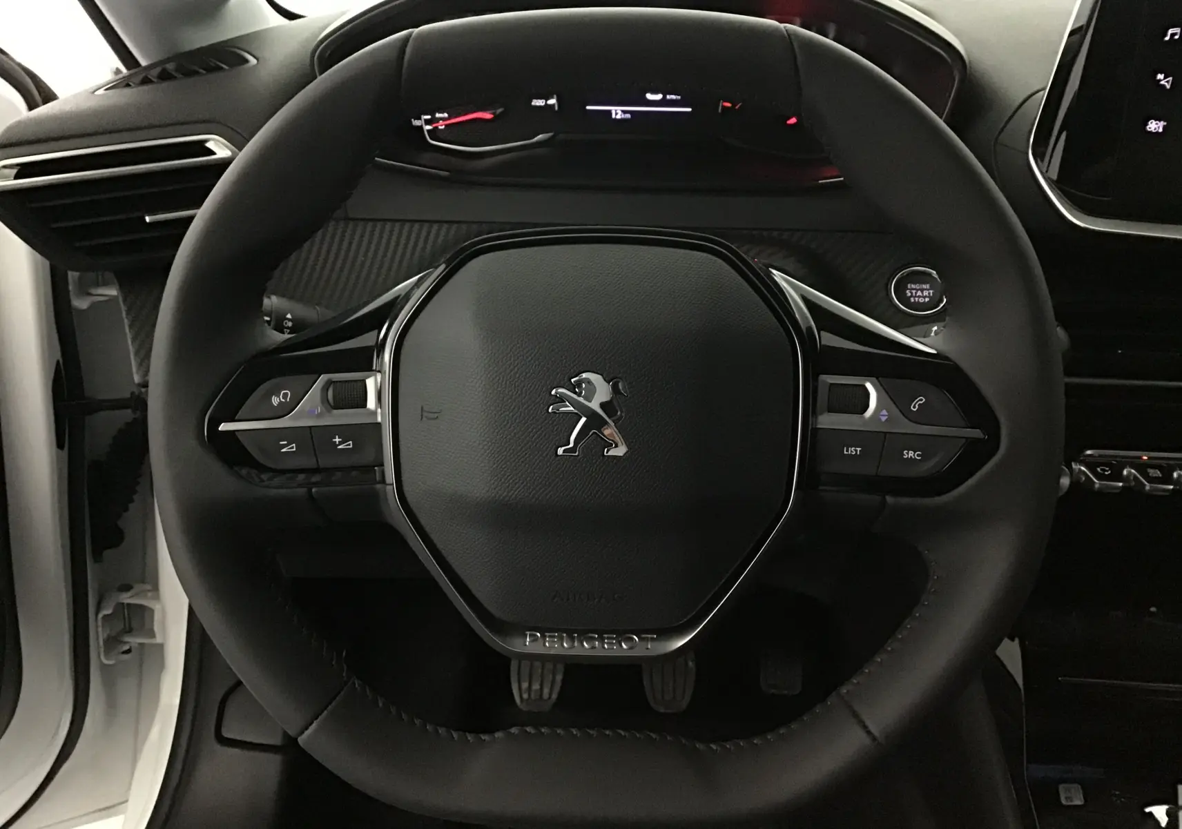 Vue rapprochée du volant noir de la Peugeot 208 blanche 2024 avec commandes intégrées et tableau de bord digital.