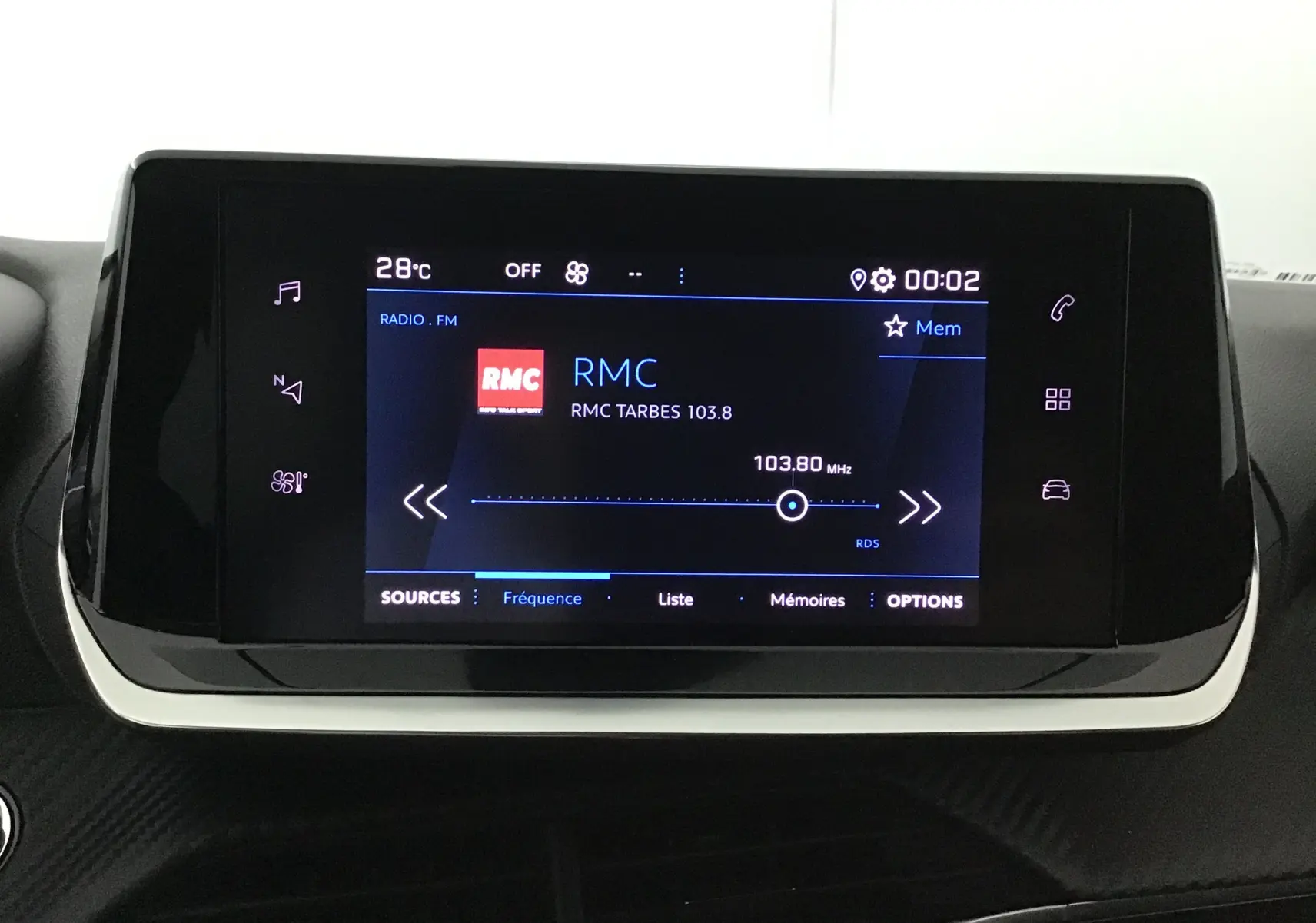 Écran tactile central du tableau de bord du Peugeot 208 blanc 2024 affichant la radio FM RMC à 103,8 MHz