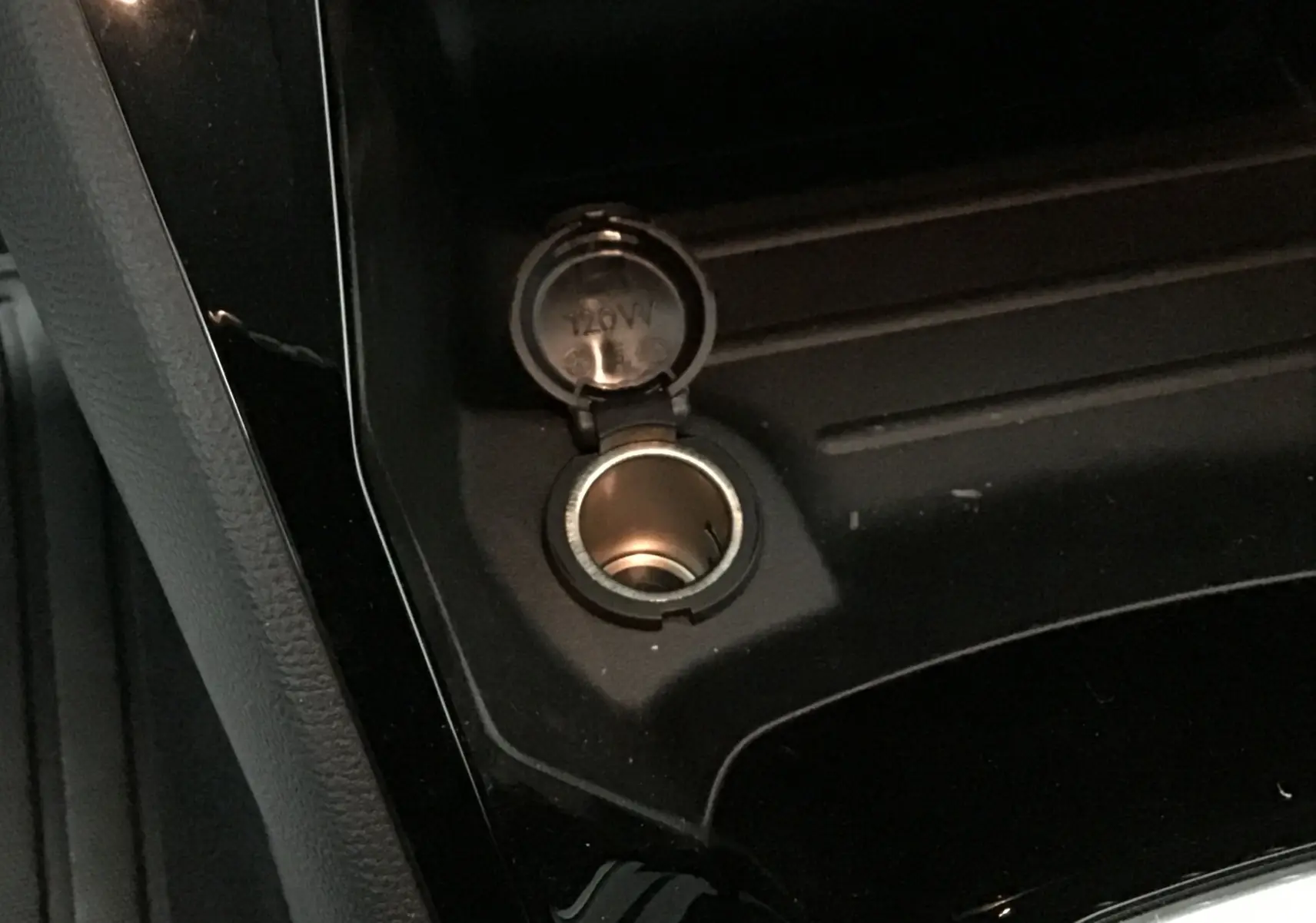 Prise 12V ouverte sur la console centrale noire d'une Peugeot 208 blanche essence 2024, version Allure Pack.