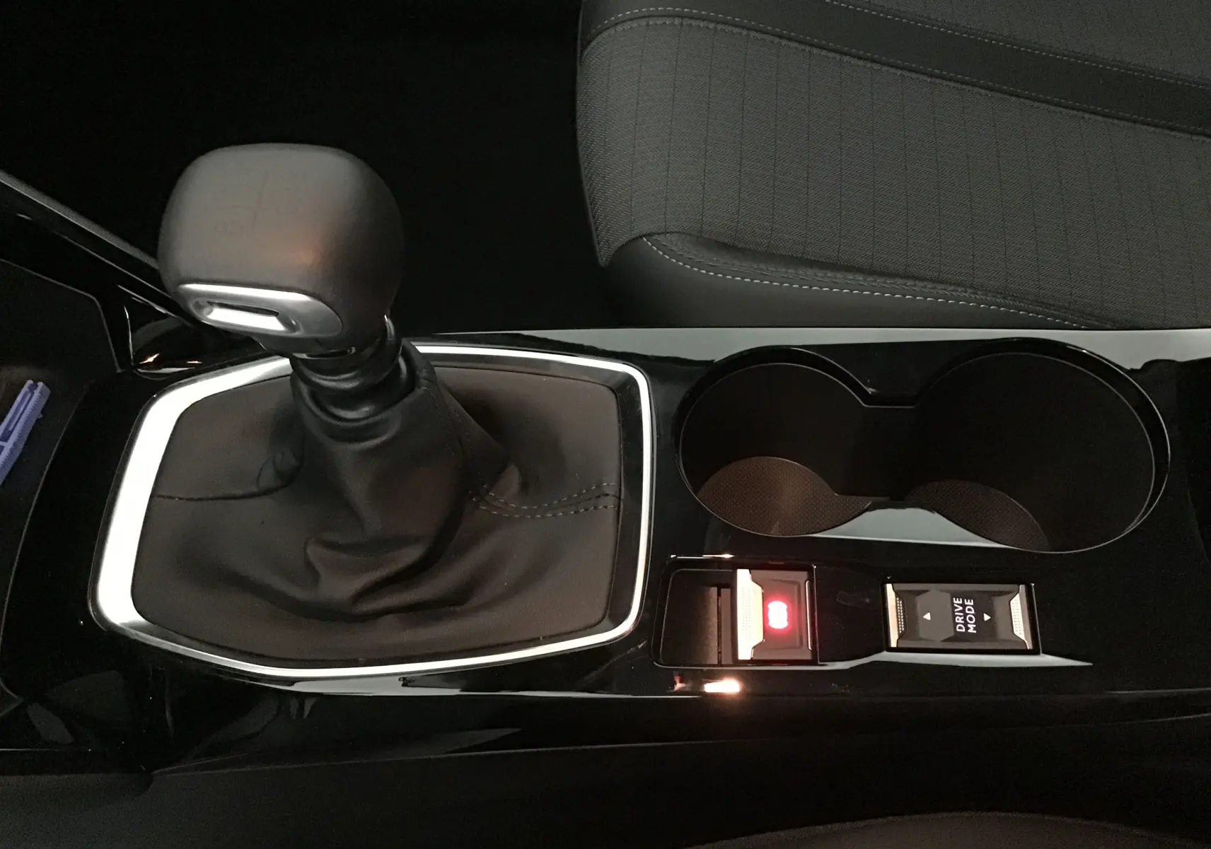 Gros plan sur la console centrale noire de la Peugeot 208 blanche 2024, mettant en valeur le levier de vitesse manuel et les porte-gobelets.