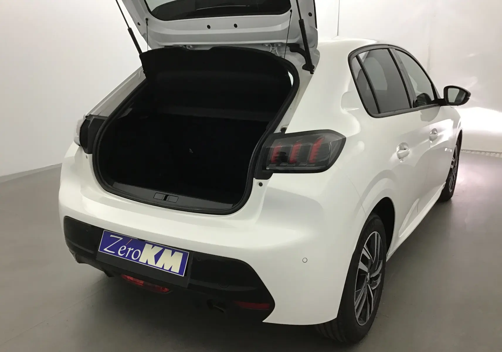 Vue 3/4 arrière droite d'une Peugeot 208 blanche 2024 avec coffre ouvert et feux arrière distinctifs teintés.