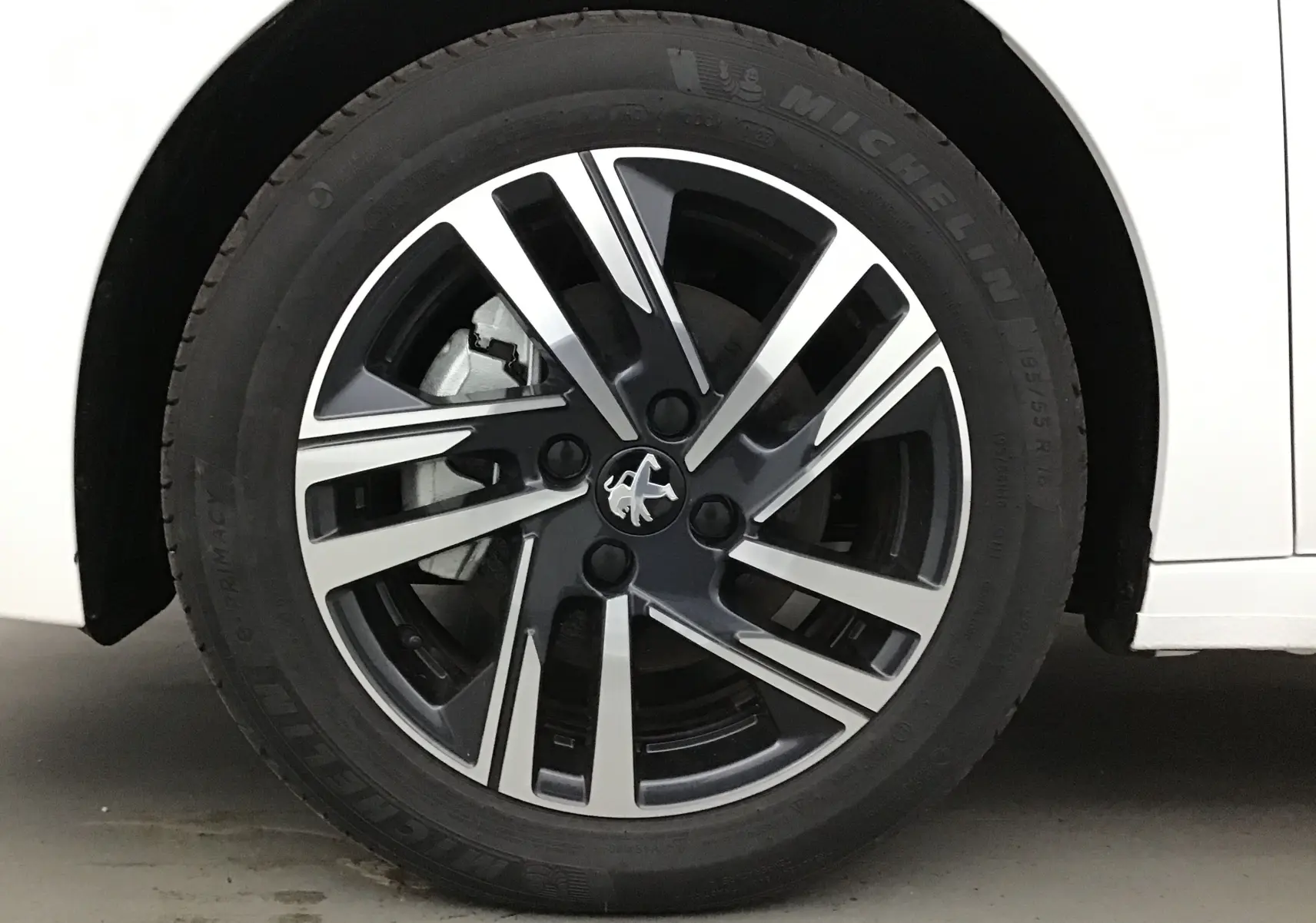 Gros plan sur la roue avant gauche blanche d'une Peugeot 208 1.2 PureTech 100 Allure Pack avec jante alliage noire et argent.