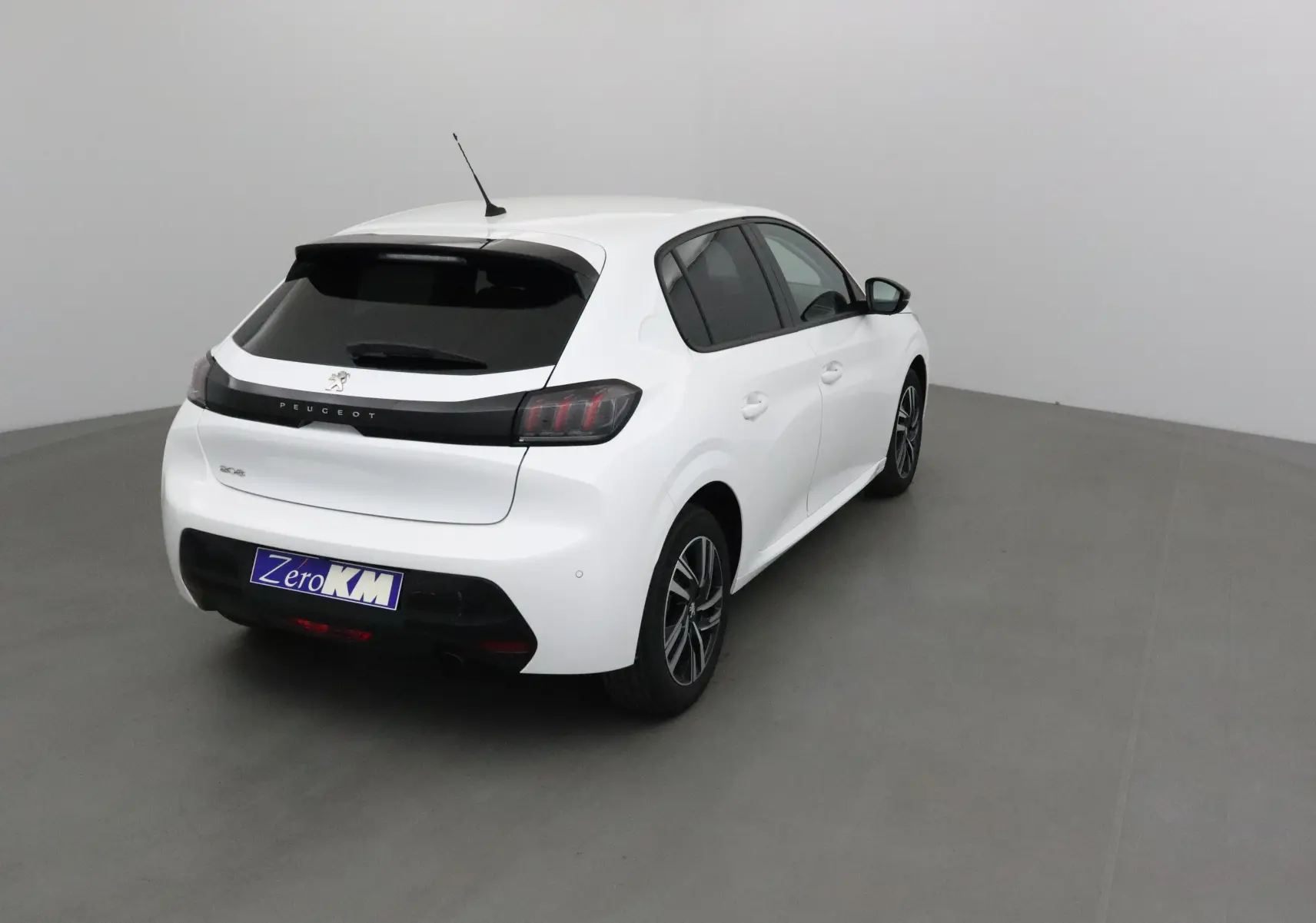 Vue 3/4 arrière droite d'une Peugeot 208 blanche 2024 avec vitres teintées et jantes alliage noires.
