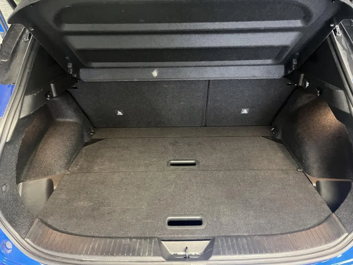 Coffre ouvert du Nissan Qashqai bleu 2024, vue arrière montrant le plancher plat et les parois intérieures noires.