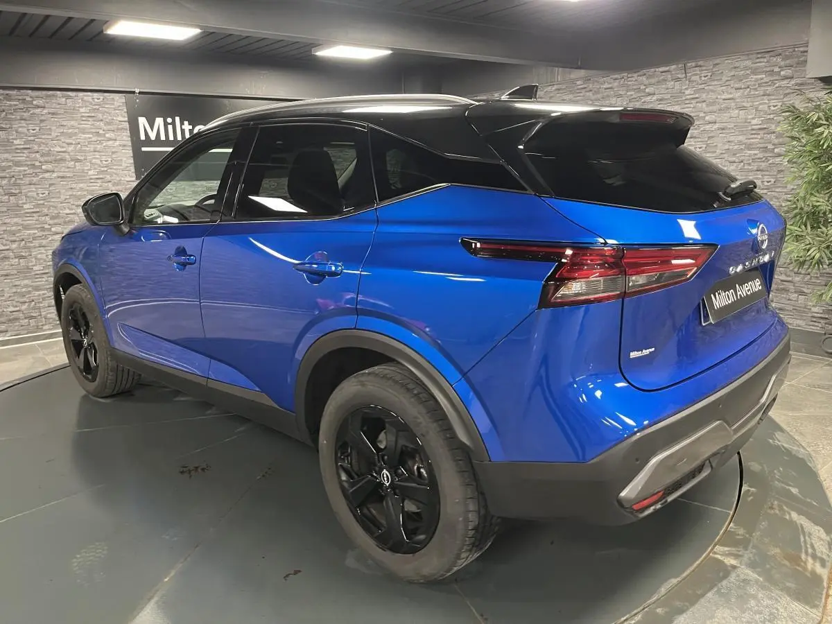 Vue 3/4 arrière droite du Nissan Qashqai 2024 bleu avec toit noir et jantes alliage noires en intérieur showroom.